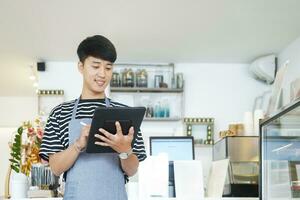 Cheerful young Asian man entrepreneur standing at counter in his own coffee shop photo