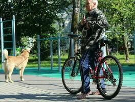 Sankt Petersburg Russia - 07 23 2023 A man on a bicycle walks his dog in a city park. People and their pets. photo