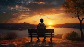 A bench in front of a sunset view with a boy sitting on it. silhouette concept photo