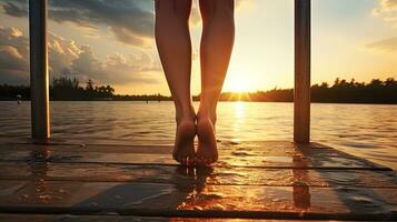 cerca arriba de niña s piernas en de madera muelle puesta de sol en río playa. silueta concepto foto