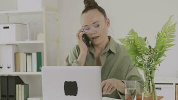 uma mulher dentro óculos sentado às uma escrivaninha com uma computador portátil e falando em a telefone video