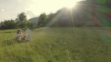 a girl and a boy holding a house cutout sitting in the grass on a hill video