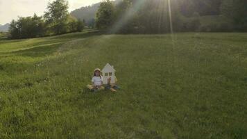 ein Mädchen und ein Junge halten ein Haus ausgeschnitten Sitzung im das Gras auf ein Hügel video