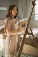 joven mujer artista pintura en lona en el caballete a hogar en dormitorio - Arte y creatividad concepto foto