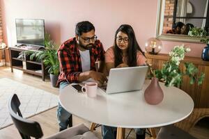 milenario indio marido y esposa haciendo Doméstico papeleo, contabilidad trabajo y revisando papel facturas, ingresos a ordenador portátil computadora, utilizando en línea calculadora - económico crisis concepto foto