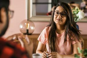 Happy couple eating breakfast and talking at dining table in morning. Indian girl and latino guy. Relationship and diversity concept photo