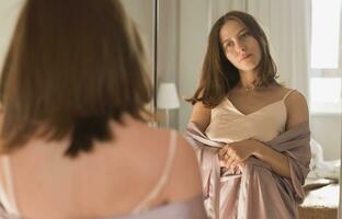 Happy morning portrait. Attractive young woman looking in mirror at her apartment - wake up and new day photo