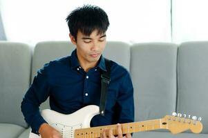 Guitarist playing guitar on sofa at home Practicing guitar at home Relax by playing stringed instruments. photo