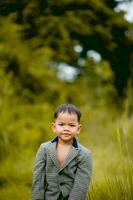 linda pequeño chico un bien vestido chico en un traje en un patio interior con un césped y mirando para alguna cosa interesante. foto