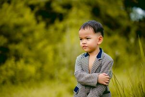 linda pequeño chico un bien vestido chico en un traje en un patio interior con un césped y mirando para alguna cosa interesante. foto