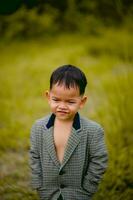 linda pequeño chico un bien vestido chico en un traje en un patio interior con un césped y mirando para alguna cosa interesante. foto