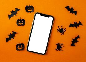 Mockup, smartphone, paper black bats, spiders and pumpkins on orange background. Halloween background. photo