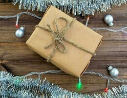 nuevo años regalo. un regalo en arte papel, un guirnalda, oropel y Navidad pelotas en un de madera antecedentes. foto