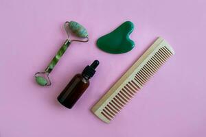 Jade massagers, comb and bottle for cosmetics on a pink background. Background with copy space. photo