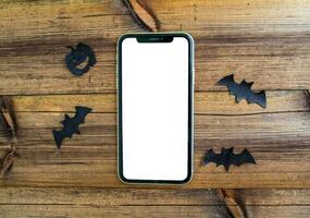 Mockup, smartphone, paper black bats and pumpkin on a wooden table. Halloween background. photo