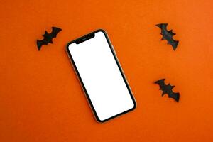 Mockup, smartphone and paper black bats on orange background. Halloween background. photo