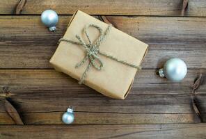 nuevo años regalo. un regalo en arte papel y Navidad pelotas en un de madera antecedentes. foto