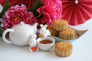 Chinese Mid-Autumn Festival concept made from mooncakes, tea decorated with plum blossom, red paper fans and rabbits isolated on white background. photo