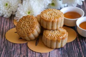 Chinese Mid-Autumn Festival concept made from mooncakes, tea decorated with Chrysanthemum blossom  on wooden background. photo