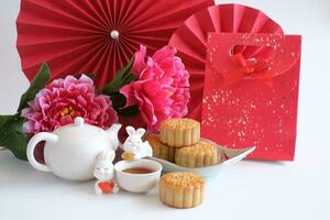 Chinese Mid-Autumn Festival concept made from mooncakes, tea decorated with plum blossom, red paper fans, red bag and rabbits isolated on white background. photo