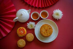 Chinese Mid-Autumn Festival concept made from mooncakes, tea decorated with Chrysanthemum blossom, rabbit and red paper fans on red background. photo