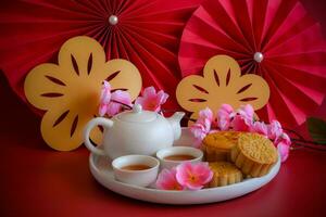 Chinese Mid-Autumn Festival concept made from mooncakes, tea decorated with plum blossom, rabbit and red paper fans on red background. photo