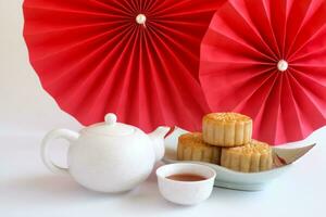 Chinese Mid-Autumn Festival concept made from mooncakes, tea decorated with plum blossom, red paper fans and rabbits isolated on white background. photo