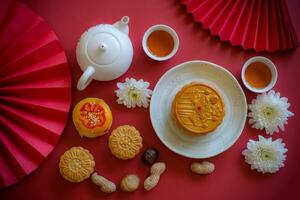 Chinese Mid-Autumn Festival concept made from mooncakes, tea decorated with Chrysanthemum blossom, rabbit and red paper fans on red background. photo