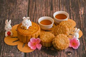 Chinese Mid-Autumn Festival concept made from mooncakes, tea decorated with plum blossom and rabbits on wooden background. photo