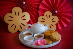 Chinese Mid-Autumn Festival concept made from mooncakes, tea decorated with plum blossom, rabbit and red paper fans on red background. photo