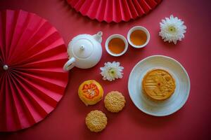 Chinese Mid-Autumn Festival concept made from mooncakes, tea decorated with Chrysanthemum blossom, rabbit and red paper fans on red background. photo