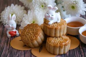 chino mediados de otoño festival concepto hecho desde tartas de luna, té decorado con crisantemo florecer y Conejo en de madera antecedentes. foto