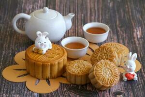 chino mediados de otoño festival concepto hecho desde tartas de luna, té decorado con ciruela florecer y conejos en de madera antecedentes. foto