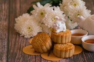 chino mediados de otoño festival concepto hecho desde tartas de luna, té decorado con crisantemo florecer y Conejo en de madera antecedentes. foto