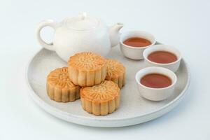 Chinese Mid-Autumn Festival concept. Mooncakes and hot tea pot in plate isolated on white background. Chinese mid autumn festival food. photo