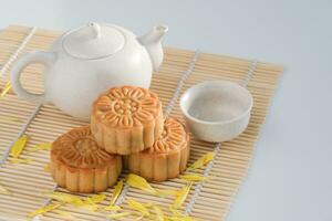 Chinese Mid-Autumn Festival concept made from mooncakes in plates and hot tea pot on bamboo mat with the white background. Chinese mid autumn festival food. photo