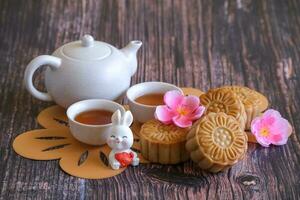 Chinese Mid-Autumn Festival concept made from mooncakes, tea decorated with plum blossom and rabbits on wooden background. photo