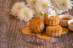 Chinese Mid-Autumn Festival concept made from mooncakes, tea decorated with Chrysanthemum blossom and rabbit on wooden background. photo