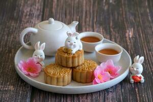 Chinese Mid-Autumn Festival concept made from mooncakes, tea decorated with plum blossom and rabbits on wooden background. photo