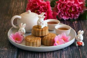 Chinese Mid-Autumn Festival concept made from mooncakes, tea decorated with plum blossom and rabbits on wooden background. photo