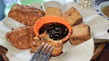 Fried tempeh, fried tofu, soy sauce and a little chili sauce in a bowl photo