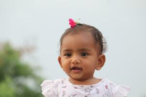 Cute  Indian Asian  baby girl looking at camera with pink flower in her hair photo