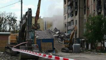 Construction work on the demolition of multi-storey apartments. Fence made of red and white warning tape. Excavator with hydraulic crusher at house demolition. Ukraine, Irpin - May 12, 2023. video