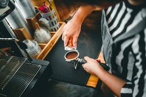 Barista holding portafilter and coffee tamper making an espresso coffee in cafe photo