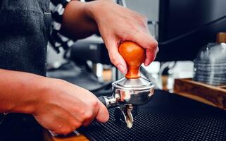 Close-up of hand Barista cafe making coffee with manual presses ground coffee using a tamper at the coffee shop photo