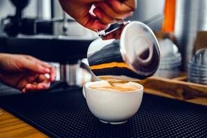 de cerca de el mano de un profesional barista en un café tienda haciendo torrencial al vapor Leche dentro el café taza haciendo latté menú foto