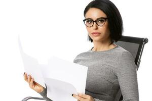 Pensive young business woman in glasses sitting on chair with paper documents. Isolated over white background. Achievement business career concept. photo