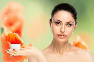 Skincare concept.Young pretty woman holding cosmetic cream jar over flowered blurred background photo