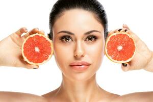 Healthy food concept. Beautiful young woman holding piece of grapefruit close to face, isolated over white background photo