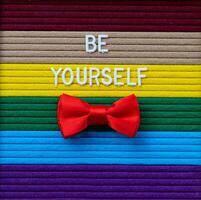 a red bow tie sits on a rainbow striped background with words Be yourself photo